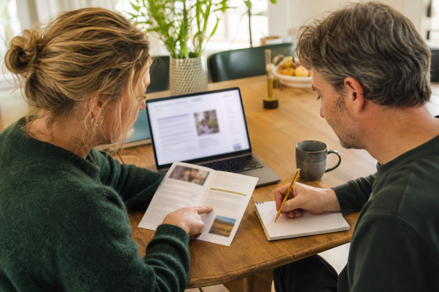 Twee mensen vergelijken informatie op een laptop en een papieren folder